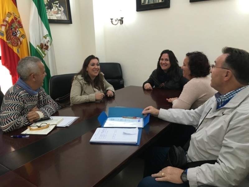 Reunión en una oficina con bandera española y andaluza, participantes en una discusión formal.