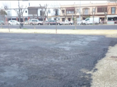 Una calle desierta con asfalto recién pavimentado. En el fondo, se pueden ver edificios y vehículos estacionados, indicando que la zona está en proceso de construcción o mantenimiento.