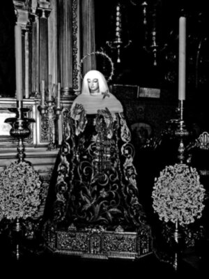 Una estatua religiosa en blanco y negro, con detalles elaborados y una candelabro al fondo.