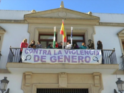 Manifestación contra la violencia de género en un balcón con banderas y pancarta.