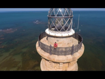 Un hombre se sienta en el borde del faro, disfrutando de la vista panorámica sobre el mar y las islas.