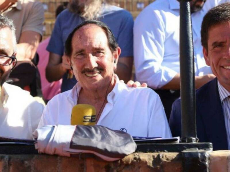 Dos hombres sonrientes, uno con micrófono, en un evento público.