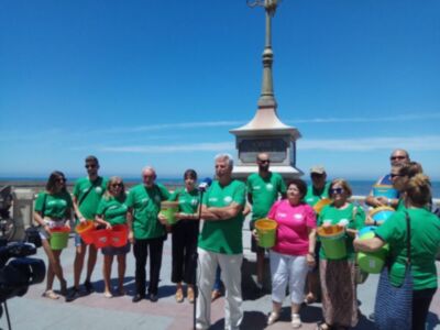 Equipo de voluntarios en verde con cubos de limpieza, frente a un monumento al aire libre.