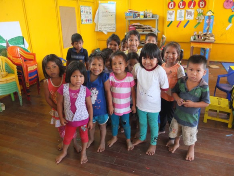 Niños sonrientes en una escuela infantil con decoración educativa en el fondo.