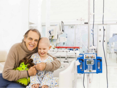 Un niño con cáncer sonríe con su padre en un hospital, rodeados de tecnología médica.