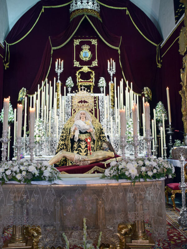 Altar con estatua de la Virgen María en trono, adornado con velas, flores y decoración dorada.