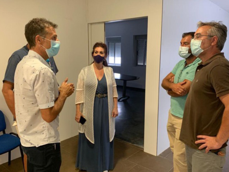 A cuatro personas en una sala de espera, todos con mascarillas. La escena parece ser un encuentro o reunión formal en un entorno institucional, posiblemente una oficina o consultorio médico.