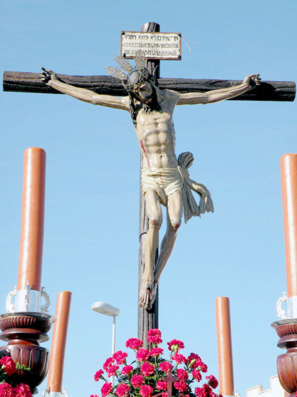 Representación de la crucifixión de Jesús con flores rojas en primer plano y velas detrás.