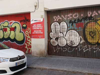 Vehículo blanco aparcado frente a un garaje con murales de graffiti.