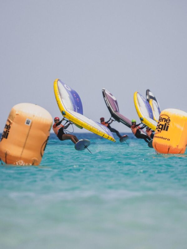Una emocionante escena de windsurfing en el mar, con surfistas volando sobre sus tablas y un cielo claro.