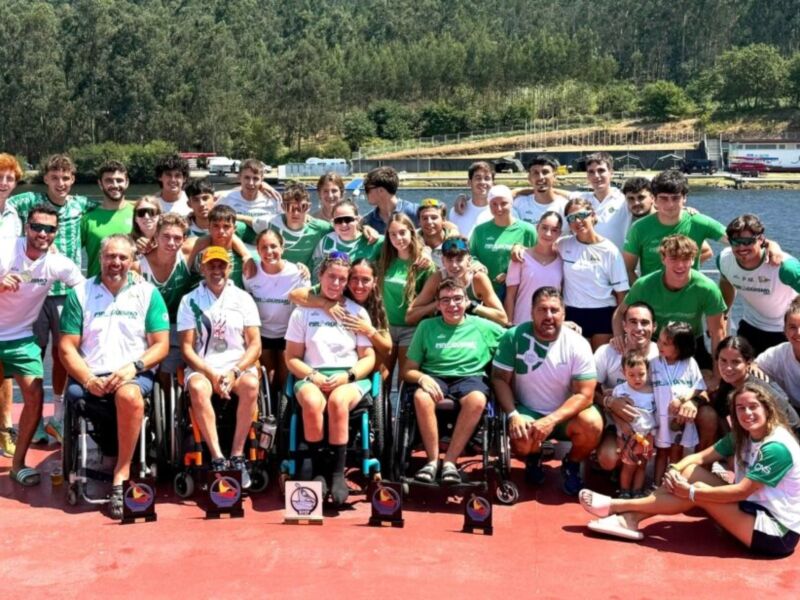 Una gran cantidad de personas en camisetas verdes y blancas posan para una foto en un embarcadero, con vehículos de fondo.
