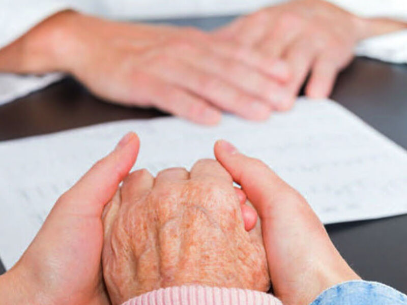 Manos de un adulto y una anciana, posiblemente en una consulta médica o terapéutica. La escena sugiere un momento de apoyo y cuidado.