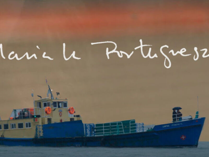 Barco de carga en el mar con banderas, texto "Maria Le Portugal" sobre fondo nublado.
