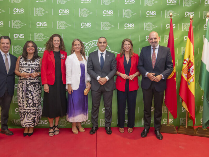 Una imagen de una celebración formal con siete personas posando frente a un fondo verde con el logotipo de la CNS. La escena está ambientada en una alfombra roja, y las personas están vestidas formalmente.