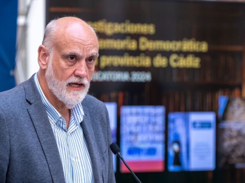 Un hombre con barba blanca habla en un escenario frente a una pantalla que muestra "Memoria Democrática Provincia de Cádiz".