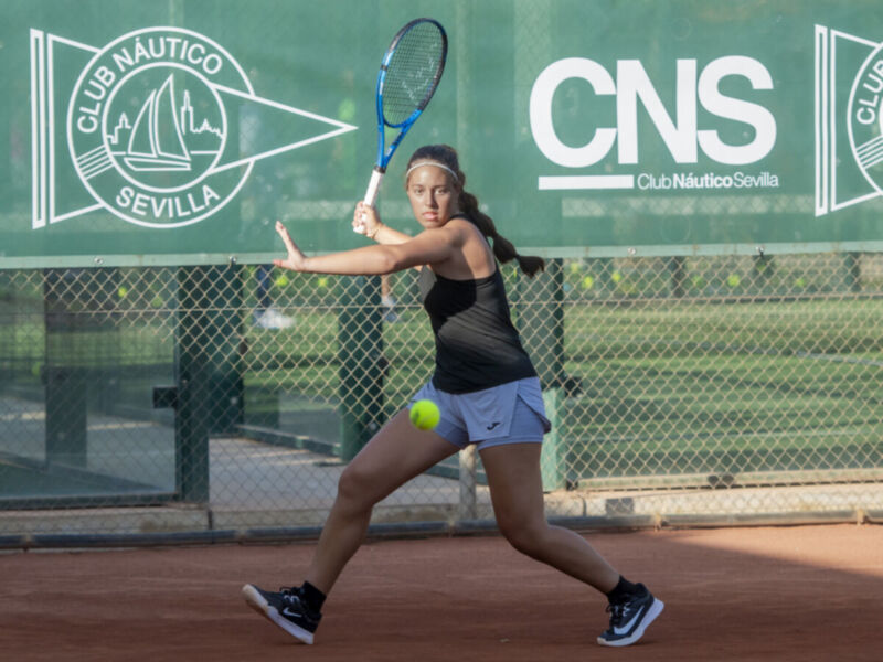Jugadora de tenis en acción, con el Club Náutico Sevilla y la marca CNS en el fondo.