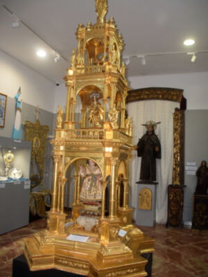 Un altar dorado en un museo, con estatuas religiosas y una cruz en la parte superior. La escena está iluminada con luces blancas.