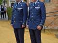 Dos oficiales militares en uniforme de gala, posando frente a una construcción con azulejos y un árbol.